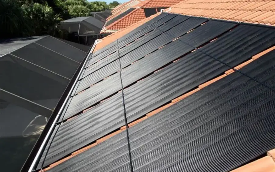 Solar pool heating collectors mounted on a tile roof, with the header pipe running along the top of the panels.